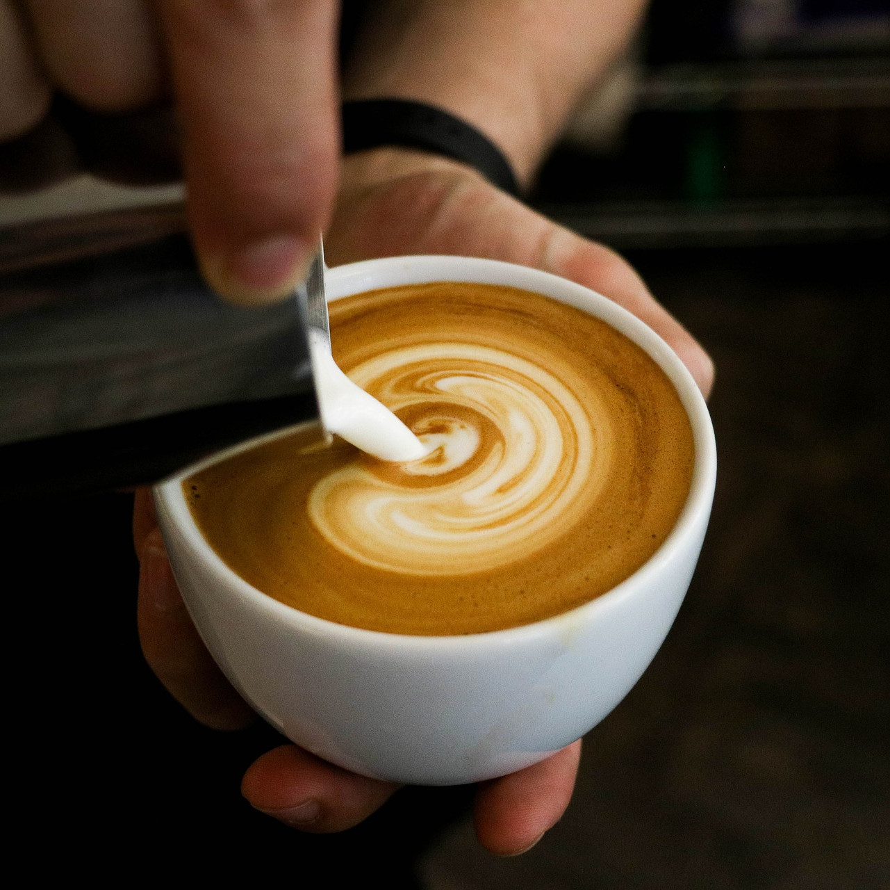 Eine Person gießt Milch in eine Tasse Kaffee.