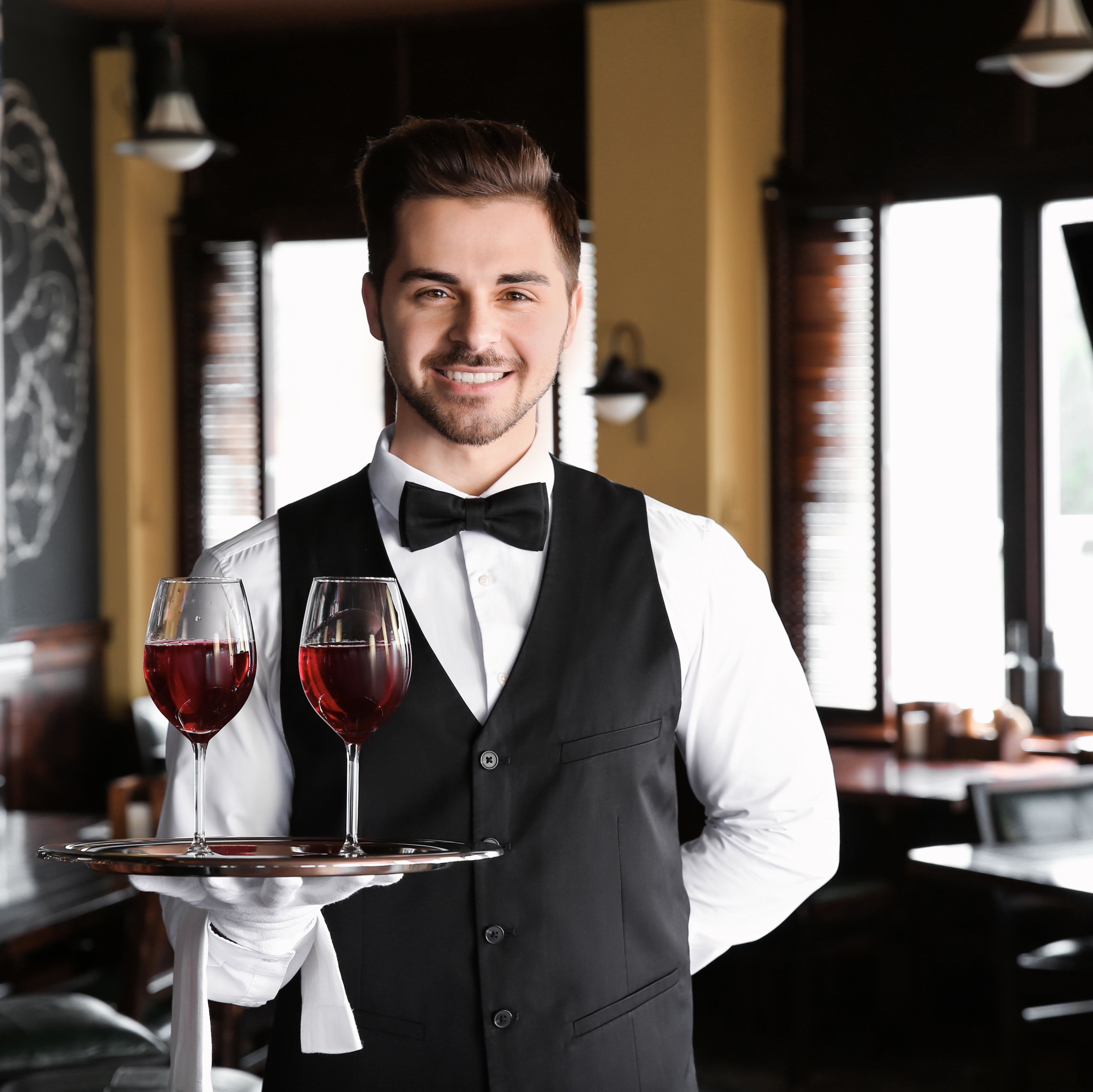 Freundlicher Kellner trägt zwei Gläser mit Rotwein auf einem Tablett