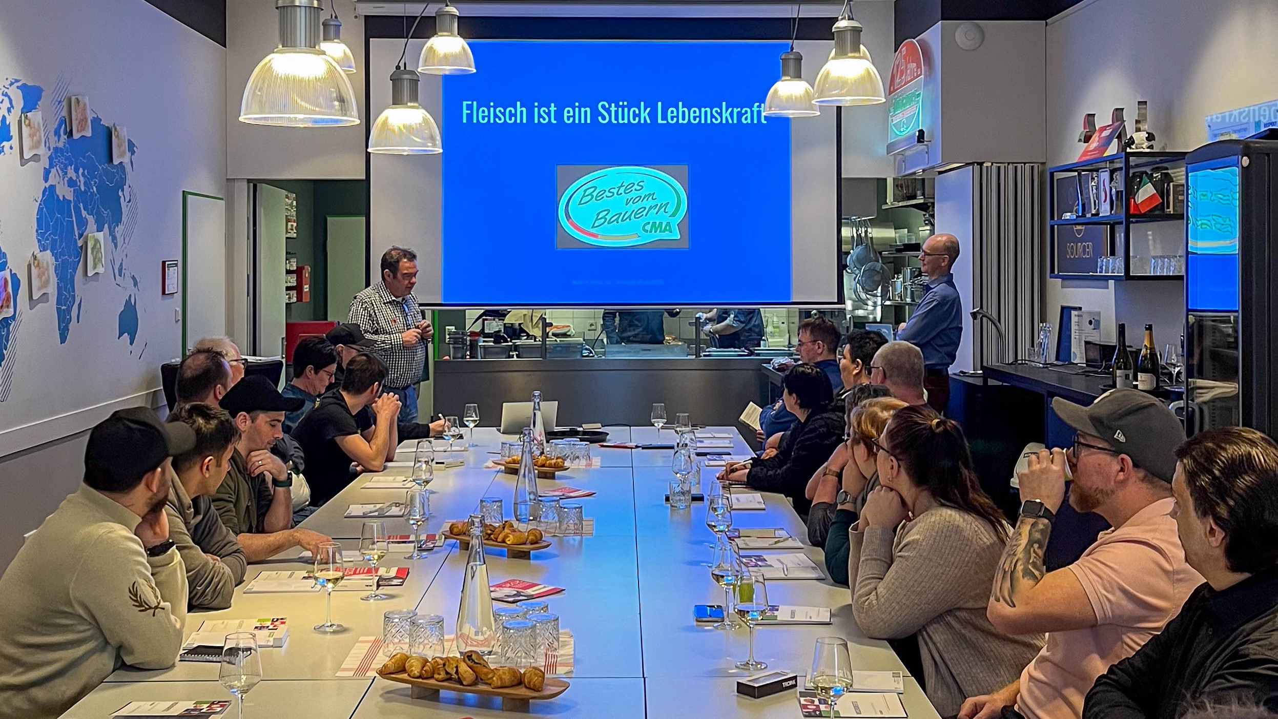 Workshop-Teilnehmer sitzen um den Tisch und hören dem Referenten zu